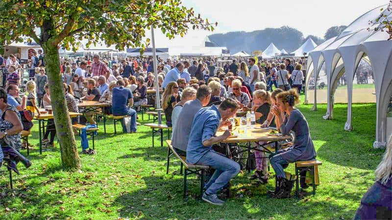 people sitting at tables eating on a wide lawn at one of the food festivals in Europe in 2023