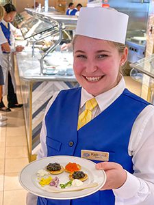 a waitress in a blue vest offering a plate of caviar aboard the Seven Seas Splendor