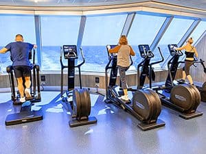 three people exercising in a gym while looking out a large window at the sea