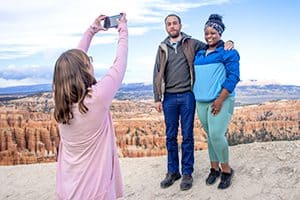 a woman in a pink sweater taking a photo of a couple in Utah National Parks