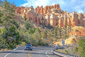 a car driving past a large colorful rock formation in one of the Utah National Parks