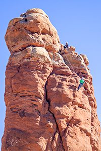 2 men rappelling down a tall rock outcrop in one of the Utah National Parks
