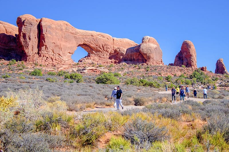 In Utah National Parks people walking past a arch in a large stone ridge