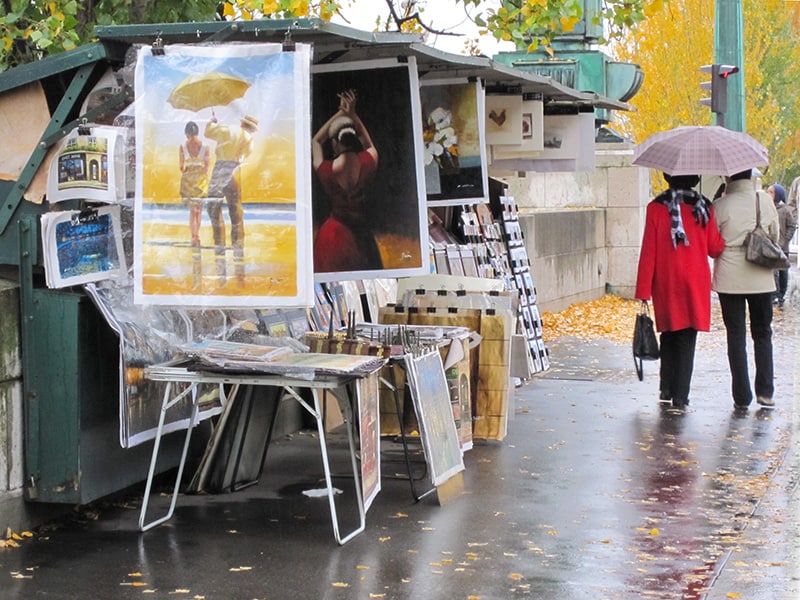 two women with an umbrella walking past a stand selling old posters