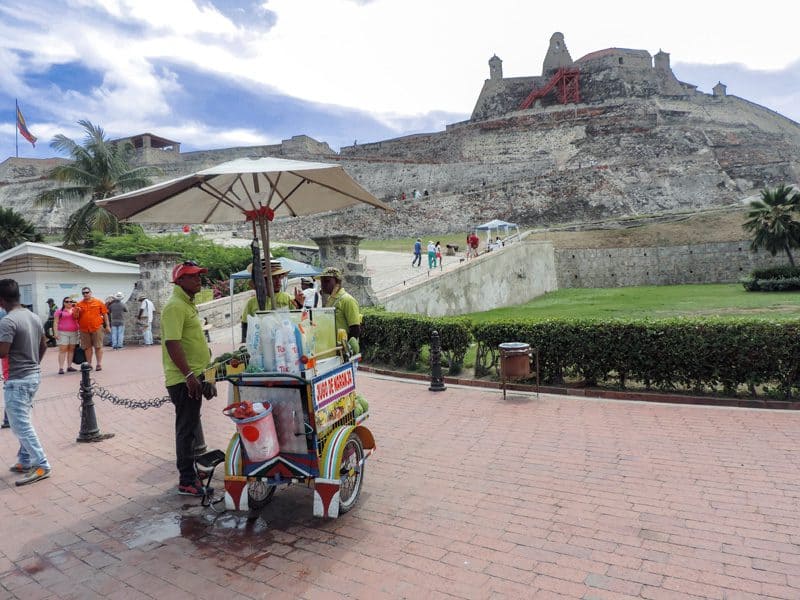 vendors with their carts standing below a huge ancient fort on a hilltop 