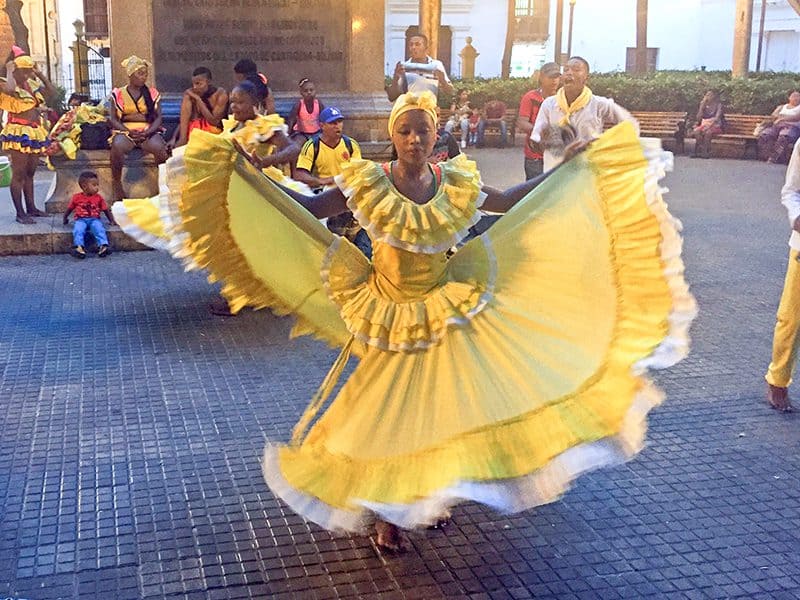 women in yellow dresses doing a folk dance in a plaza