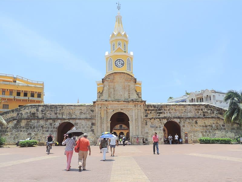 a tall yellow clock tower in a broad plazza in Cartagena Colombia