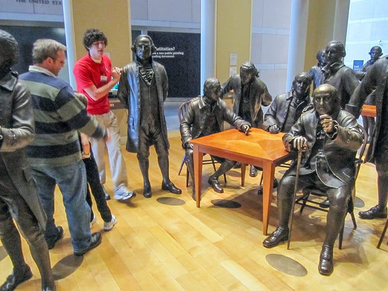 a man in a red shirt walking past a large group of statues of people