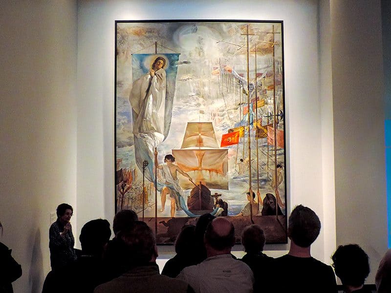people looking at a large painting  in a small museum