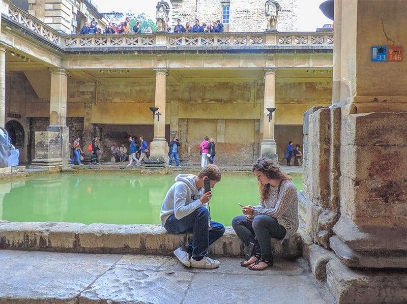 a couple sitting alongside the baths at the Roman Baths seen on a day trip from London to Bath