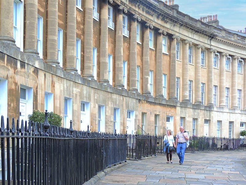 a coupkle walking past a building with large columns seen on a day trip from London to Bath