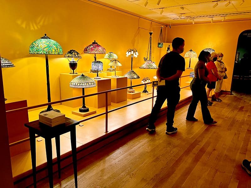 people by an exhibit of glass lamps  in a small museum