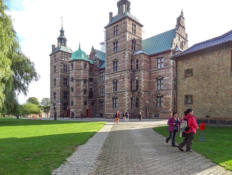 people walking through a park past an old castle