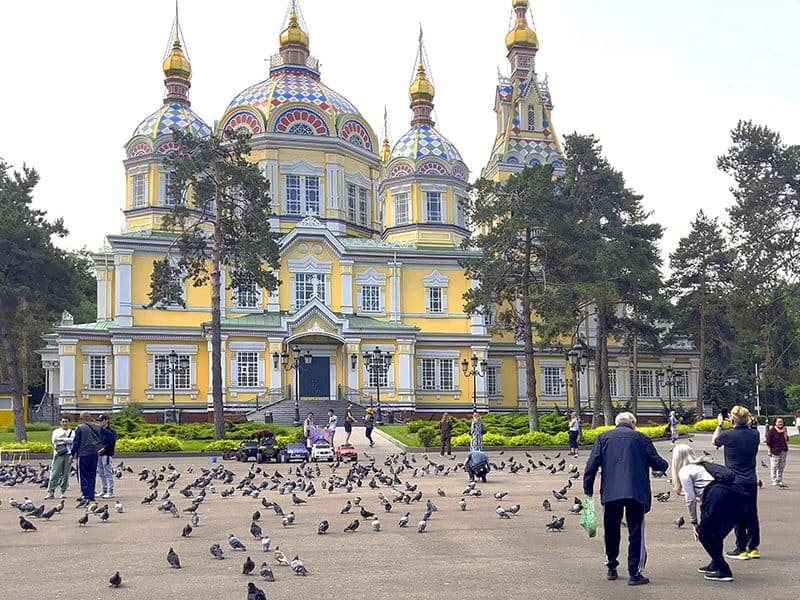 people feeding pigeons in front of an ornate yellow orthodox cathedral, seen on a visit to almaty kazakhstan