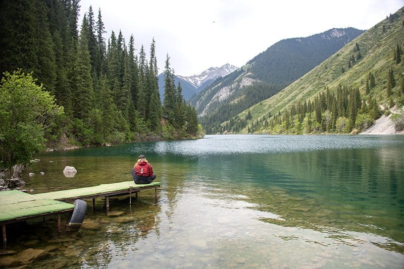 a woman in red sitting on a lakeside dock seen on a visit to almaty kazakhstan