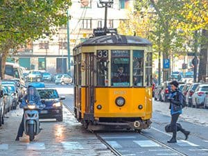 a many crossing a street in front of a yellow trolley