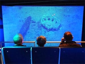 three people watching a video of about the discovery of the Titanic on the sea floor