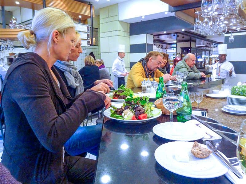 people eating at a counter with chefs standing near them