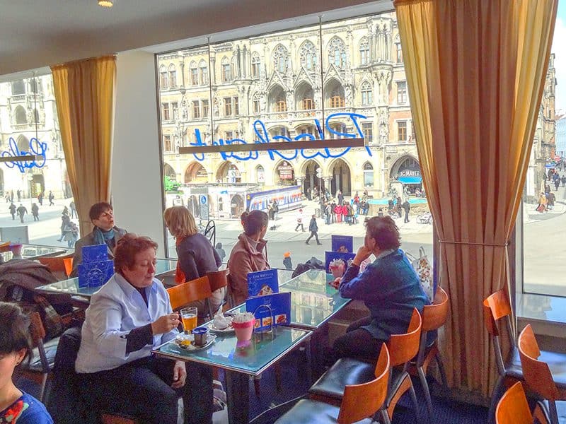 people in a restaurant looking out the windows of a broad city square