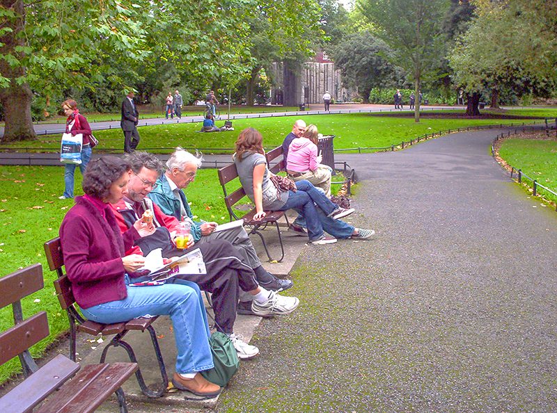 people eating lunch while sitting on a bench in a park