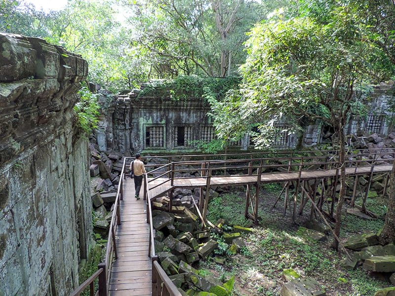 a man walking along an elevated boardwalk looking at ruins