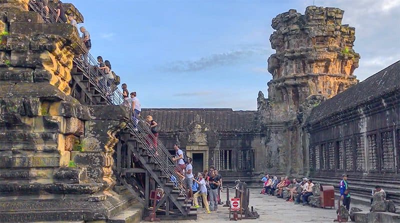 people climbing steep stairs to a temple while visiting Angkor Wat