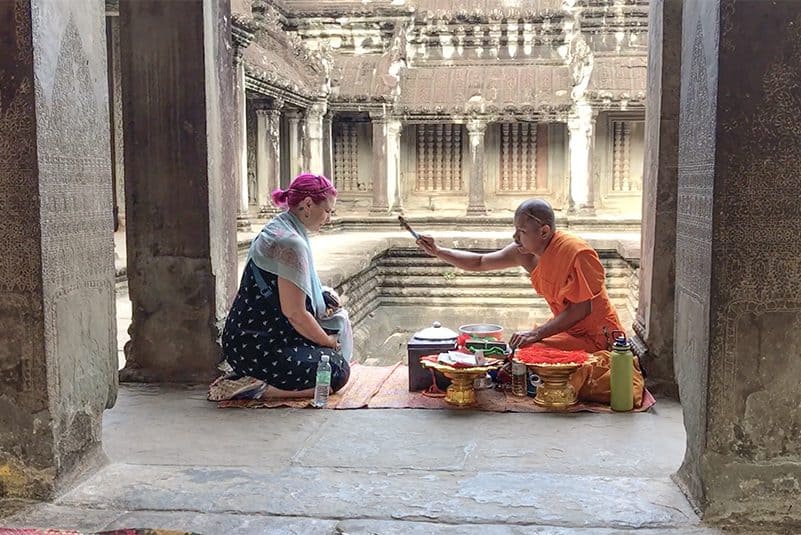 a woman being blessed by a monk while visiting Angkor Wat