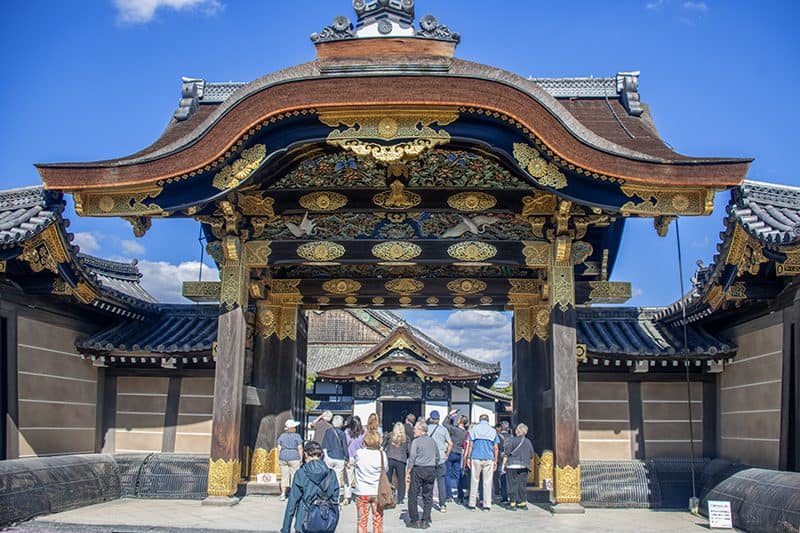 people walking under an ornate gateway to a castle - one of the things to do in Kyoto