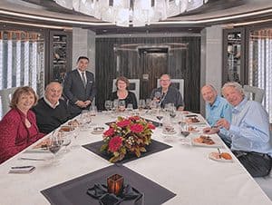 people sitting at a long table on which is a vase of red roses