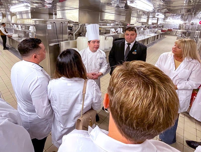 a chef talking with people on a tour of a large ship's kitchen