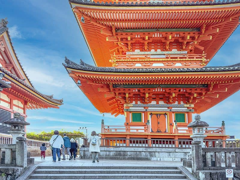 people walking below a bright red Japanese temple enjoying the Kyoto weather