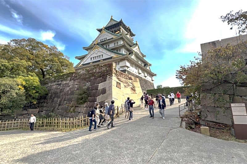 people walking beneath a huge Japanese casle on a hill