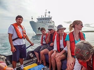 people in a small boat moving away from a ship