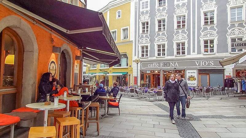 a couple walking past cafes and an ornate gray building