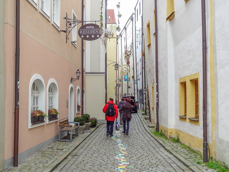 people walking down a street with a line of painted cobblestones in its center