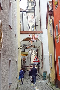 people walking along a cobblestone street with artwork hanging from a building