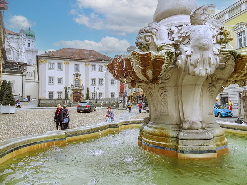 people walking by a fountain in a square in Passau Germany