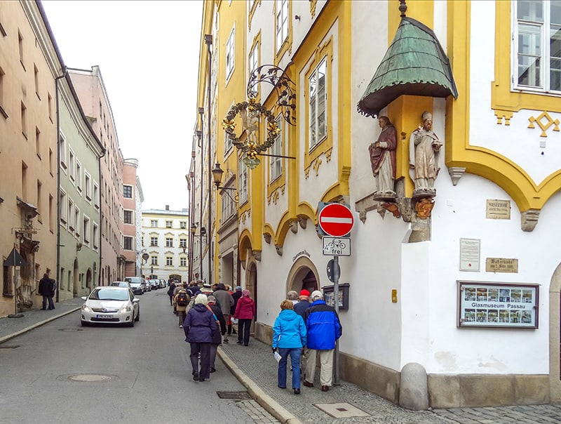 people walking past a Gothic building with statues of saints on the corner of the building