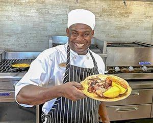 a cook serving jerked chicken  
at Sandals Dunns River Resort