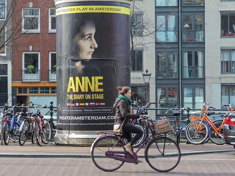 a bicyclist riding pass a large poster of Anne Frank seen during 2 days in Amsterdam