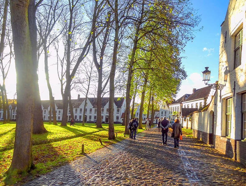 people walking through a park with white buildings surrounding the lawn - one of things to do in Bruges