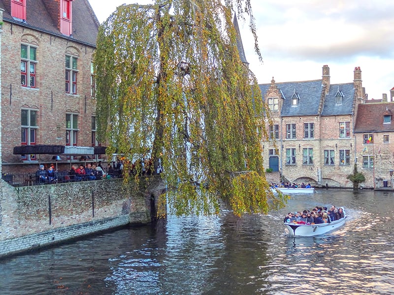 a boat filled with tourists passing people sitting in an outdoor cafe