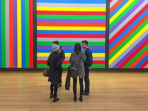 4 people standing in front of a painting with large color lines