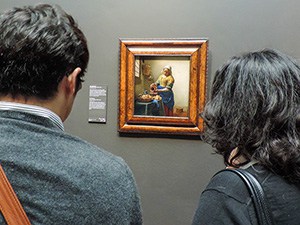 two people looking at a small painting in an ornate wood frame