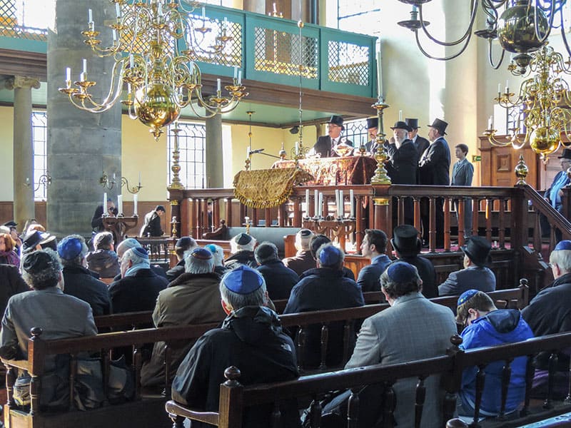 men at a service in a synagogue with large brass chandeliers hanging from the ceiling seen during 2 days in Amsterdam