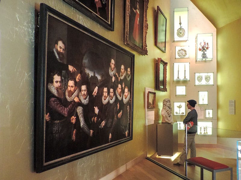 a young man looking at a larger portrait of old Dutch men 