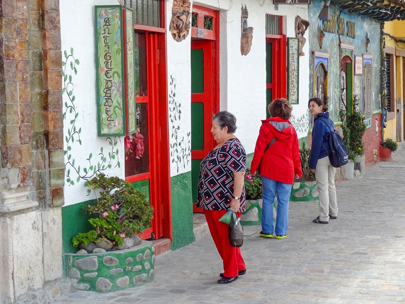people walking along a street woth colorful buildings - one of the things to do in Cuenca