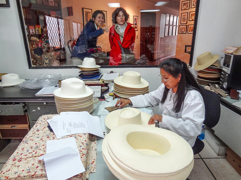 two women looking at a woman making hats