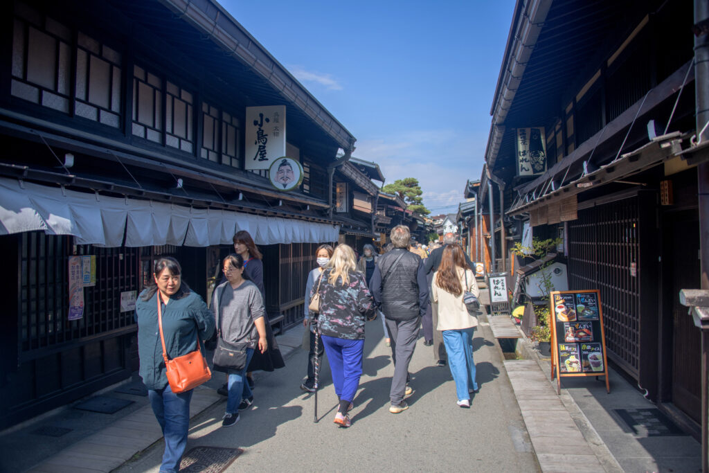 people walking along a street lined with ancient wooden buildings in Takayama's old town, one of the things to do in Japan