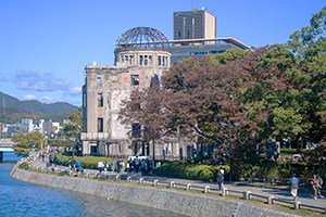 people walking along a river by an old domed building